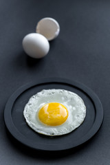 Fried egg. Close-up of fried eggs on a black plate. A whole egg and shells next to it in blur on a black background.