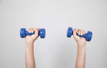 Girl hands holding dumbbells in gray background.