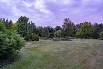 Fototapeta na wymiar During twilight, these threatening clouds create a distinct atmosphere in this beautifully landscaped garden with a great diversity of trees and flowering shrubs