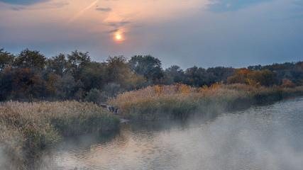 South of Russia, the vicinity of Rostov-on-Don. Autumn sunset over the grove and reeds along the river bank. Light fog over the water.