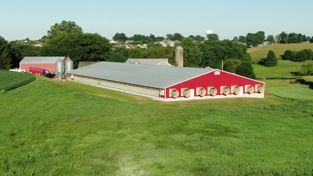 Red chicken house, pig barn with exhaust fans on summer day, stinky smelly manure bothers neighbors, residential housing development in distance