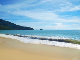 Fototapeta na wymiar Coastal waves wash a white sand. Sea foam on the crest of the wave. Empty beach. Panoramic views of the open ocean and the green promontory stretching to a horizon. Thailand. Phuket. Tropical paradise