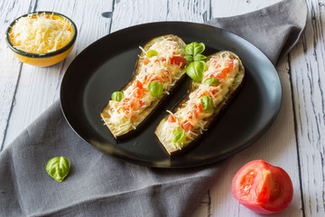 Fried eggplant stuffed with tomatoes, grated cheese, yogurt dressing and cranberries, garnished with Basil leaves on a dark plate over wooden background. Top view.