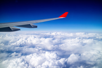 Airplane wing and aerial view during flight with clear blue sky and clouds