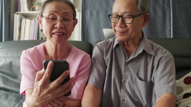 Asian old woman and old man hold mobile phone or tablet for talking and smiling on video call with son, daughter and grandchildren at home. Grandparents feel happy with communicate via internet. 