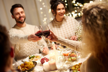 holidays, celebration and people concept - happy friends having christmas dinner at home drinking non-alcoholic red wine