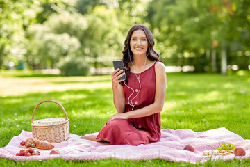 leisure and people concept - happy smiling woman with smartphone and earphones, picnic basket and...