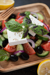 Close-up of greek salad made of feta cheese, sliced tomatoes, cucumbers, olives and fresh green basil leaves, selective focus