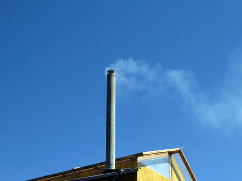 White smoke from a tall chimney located on the house, against the blue sky.