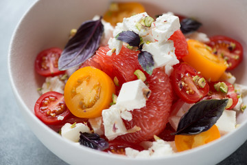 Salad with grapefruit, feta cheese, red and yellow cherry tomatoes, nuts and fresh red basil leaves, closeup, selective focus