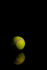 Bright Yellow Tennis Ball on dark mirror with reflections