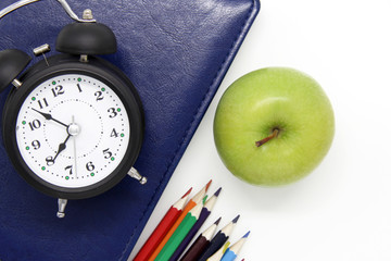 Back to school. Educational concept, office supplies. blue book, green Apple, alarm clock and colored pencils on an isolated white background. Flatly. The view from the top. A copy of the space.