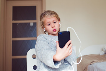 kid blogger using smartphone and video chating or streaming with friends, funny face and pose, online communication concept