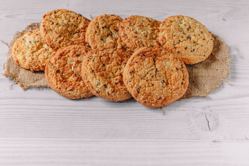 Heap of freshly baked oatmeal cookies laid out on a burlap napkin om white wood table background with copy space for text. Image design for cafe menu layout. Tasty and sweet food concept.