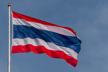The national flag of Thailand flutters in the wind against a beautiful blue sky