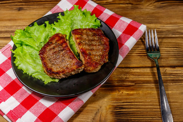 Grilled pork steaks with lettuce leaves on wooden table