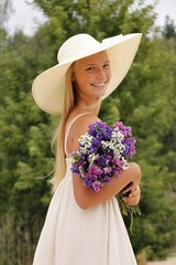 Beautiful gentle girl in hat with summer flowers