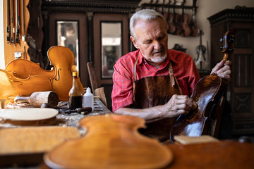 Senior carpenter craftsman polishing violin instrument in his carpenter's workshop. Creative and talented people.