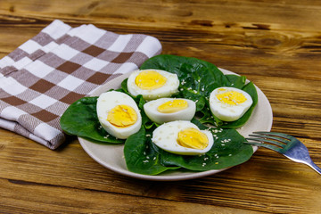 Boiled eggs with fresh spinach leaves and sesame seeds on wooden table