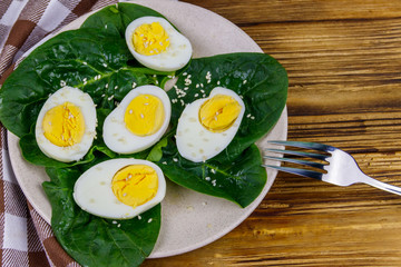 Boiled eggs with fresh spinach leaves and sesame seeds on wooden table. Top view
