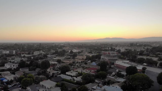 Aerial slow fly over quiet streets of the Culver city neighborhood, during sunset, with mountains in background in Los Angeles, California, USA