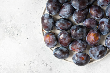 Ripe plum. A lot of plums in a white ceramic plate on a light gray table. Blue plums on a plate. Top view with space for text. Healthy fruits	
