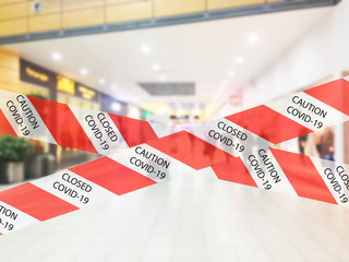 Red and white warning caution tape covid-19 warning in shopping mall. Department store interior with warning COVID-19 tape. Background shopping mall closed for COVId-19 coronavirus.