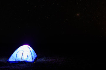 Illuminated blue tent at night under starry sky. Traveling and camping concept