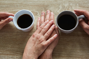 Hände berühren sich beim Kaffee trinken von oben