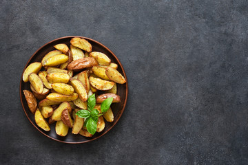 Fried potato wedges with salt and garlic in a plate on a black background. View from above.