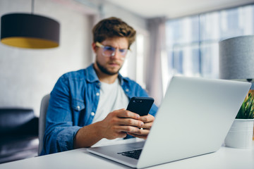 Young man with smartphone in his hands. Modern businessman at sunny office. Freelancer at work.