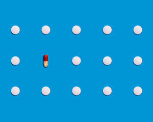 The pattern is made of white pharmaceutical tablets on a blue background. One tablet is a brown-and-white pill. Medical pharmaceutical concept. The concept of loneliness. The concept of vaccine