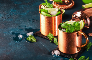 Moscow mule cocktail in copper mug with lime, ginger beer, vodka and mint. Blue table, copper bar tools, copy space