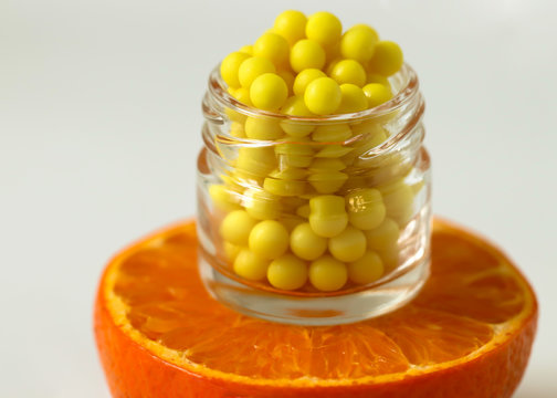 A bottle of vitamin C pills stands on a fresh slice of orange close-up on a white background. The concept of the natural supplements and vitamins