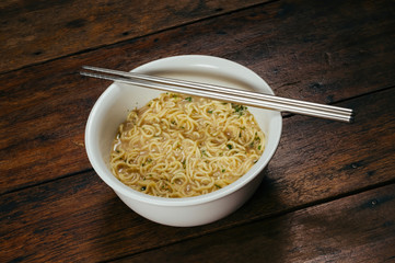 cooked instant noodle in white bowl with standless steel chopsticks on wooden table