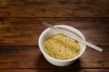 cooked instant noodle in white bowl with standless steel chopsticks on wooden table