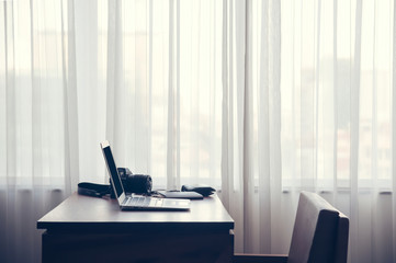 a notebook put on the wood table beside of the large window with curtain with nobody in the room of hotel or office in big city