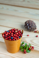 Ripe berries of lingonberry and blueberry in a decorative orange bucket on a wooden background. Berry harvest concept. Selective focus.