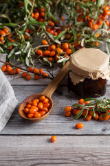 Sea-buckthorn berries in wooden spoon with jar of oil on a wooden background