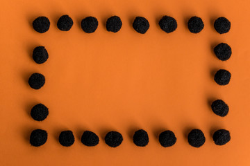 Halloween frame made of black fluffy pom-poms with copy space for text on orange background. Flat lay, top view.