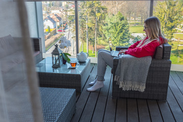 Stay at home, working in house. Woman spend free time on terrace in home clothes. Work with laptop and drinking tea. Beautiful mountain views in sunny day. Holidays time.