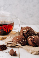 Teapot with black tea and homemade chocolate cookies on a white natural wooden background
