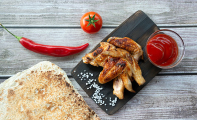Grilled chicken wings on a wooden board with sauce, tortilla and tomato. Top view
