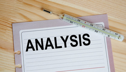 Inscription on a sheet of analysis paper, next to the thermometer. All against the background of a wooden table. A medical concept.