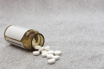 White tablets spilled out of a dark glass bottle onto a gray surface. To close. Horizontal photography, soft, selective focus.Copy space