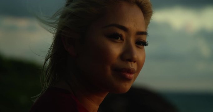 Attractive young woman looks at peace, relaxed and content as she looks at ocean and sunset in the distance while on vacation