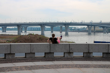 A girl with long hair in shorts does an abdominal exercise on the embankment. Sports activities...