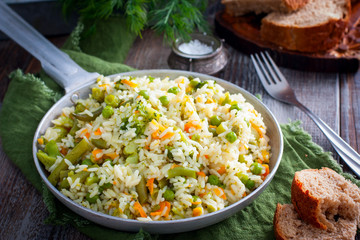 White rice with vegetables - carrots, onions, broccoli, pepper, green peas in a pan on a wooden table, horizontal