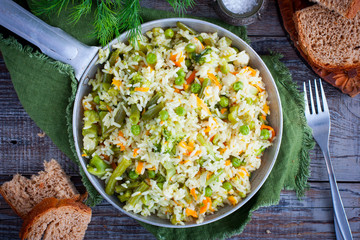 White rice with vegetables - carrots, onions, broccoli, pepper, green peas in a pan on a wooden table, horizontal