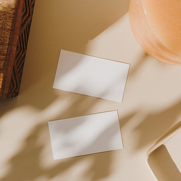 Blank paper sheet cards with mockup copy space, wooden casket and candle with sunlight shadow on beige background. Flat lay, top view minimal business brand template